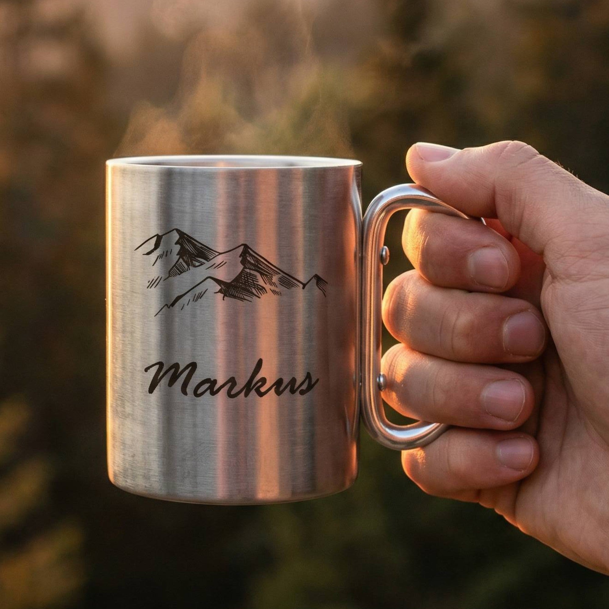 Edelstahl Camping Tasse mit Gravur Markus und Karabinergriff in der Hand vor Berglandschaft bei Sonnenuntergang, ideal für Outdoor und Wandern