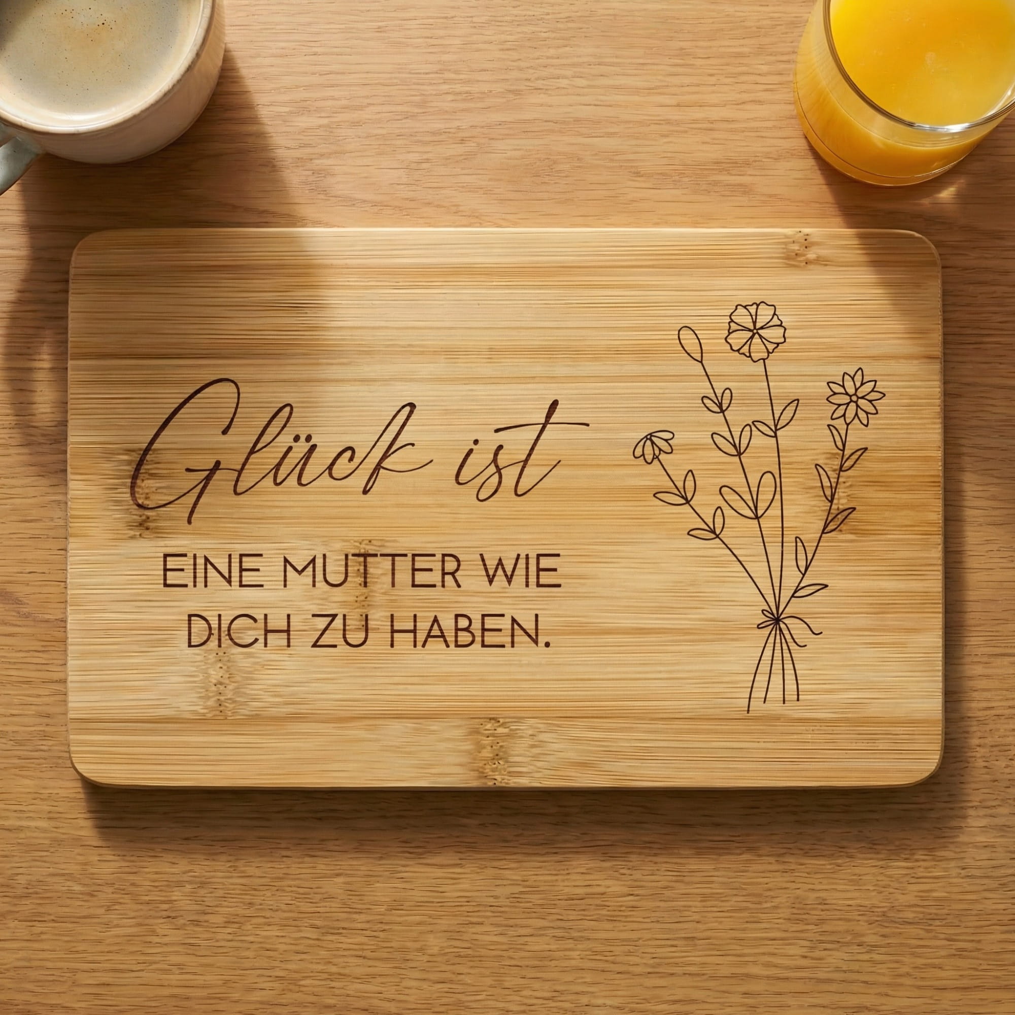 Bambus Frühstücksbrett mit Gravur „Glück ist eine Mutter wie dich zu haben“ auf Holztisch mit Croissant und Saft