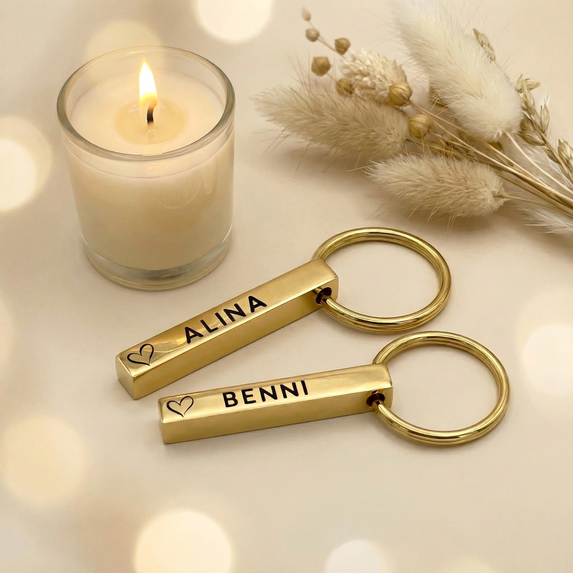 Personalisierte goldene Schlüsselanhänger für Paare mit Gravur „Alina“ und „Benni“, Herzsymbol, dekoriert mit Kerze in warmer Geschenk-Atmosphäre