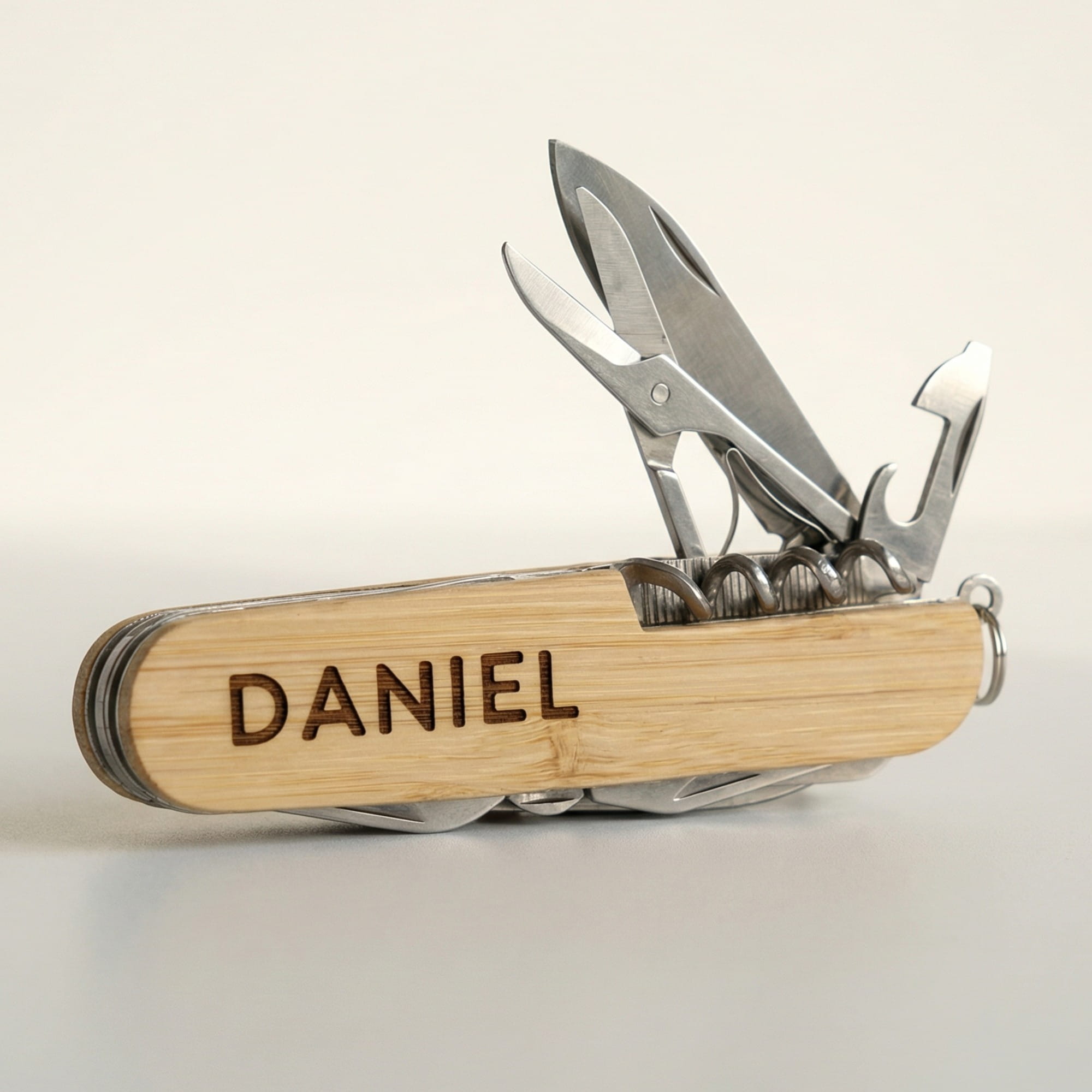 Personalisiertes Multitool Taschenmesser aus Bambus mit dunkler Namensgravur „Daniel“ und ausgeklappter Schere, Messer, Korkenzieher und Flaschenöffner